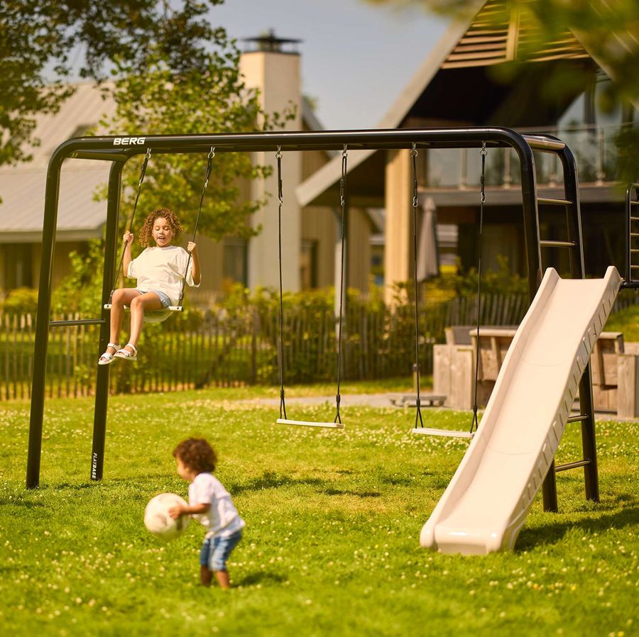 BERG PlayBase frame with a child on the swing seat, a trapeze and a slide